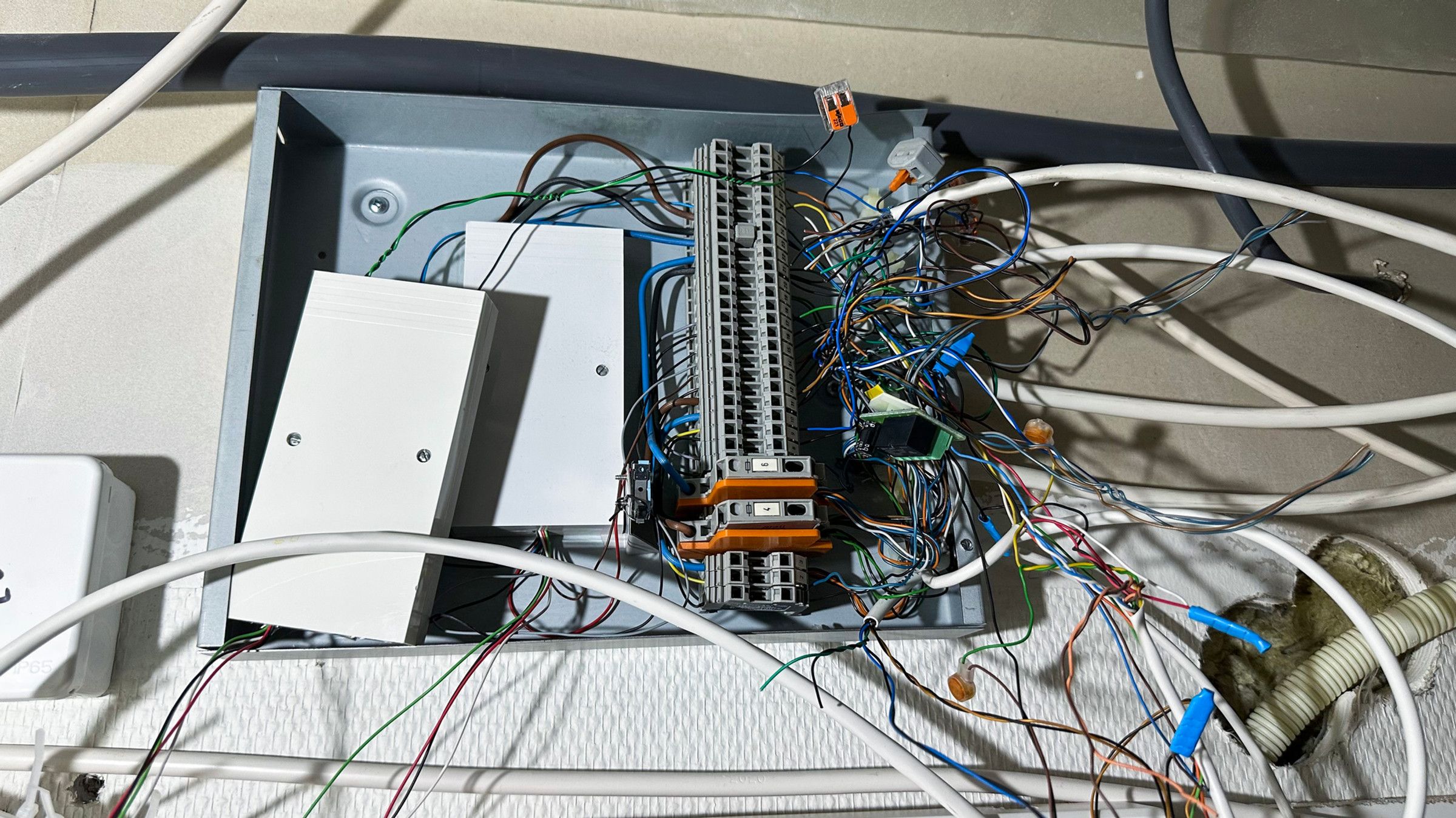 Open metal wiring box on the wall with terminal blocks and untidy wires in many colours