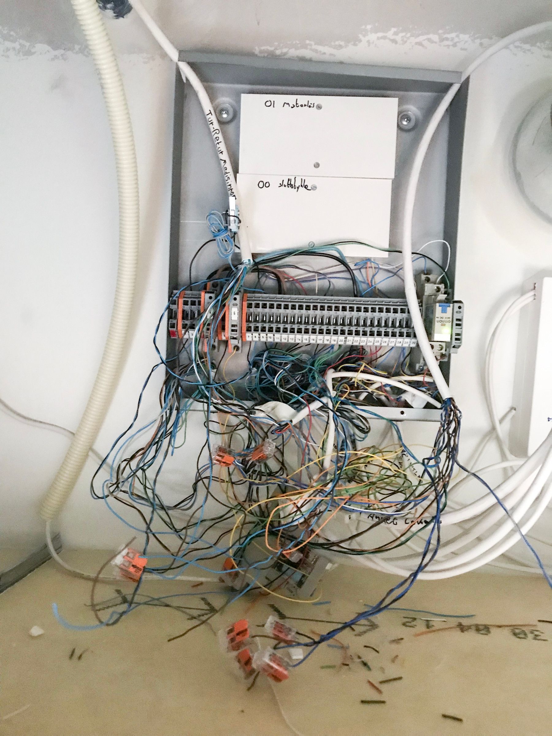 Wiring cabinet on the wall with terminal blocks and a thick bundle of loose wires hanging down, with cut wire ends on the bench