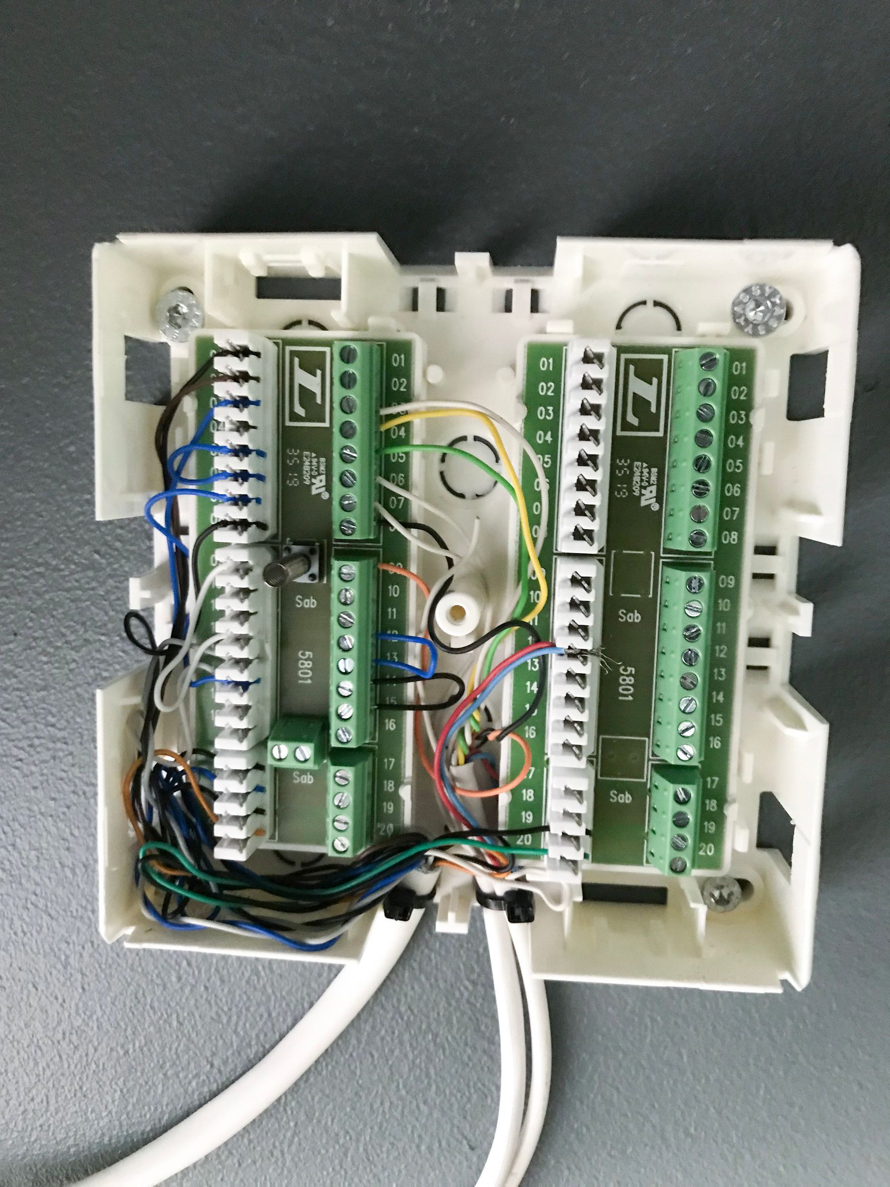 Two open white connection modules with green screw terminals and wires, with white cables underneath
