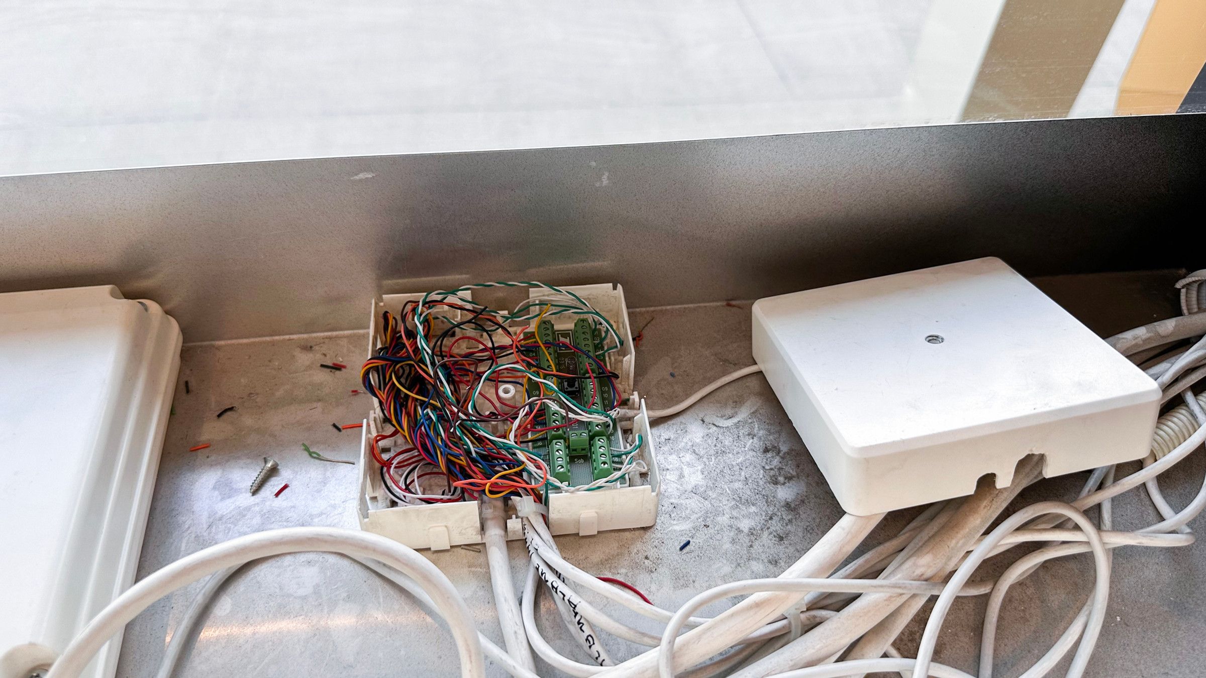 Open white wiring box on a metal shelf full of tangled, coloured wires, next to a closed box and many cables